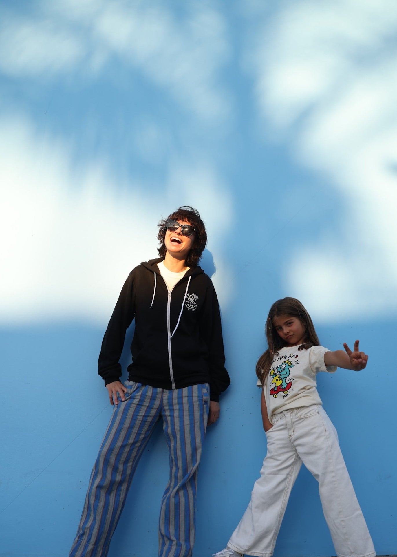 Two people posing against a blue wall with a white cloud pattern