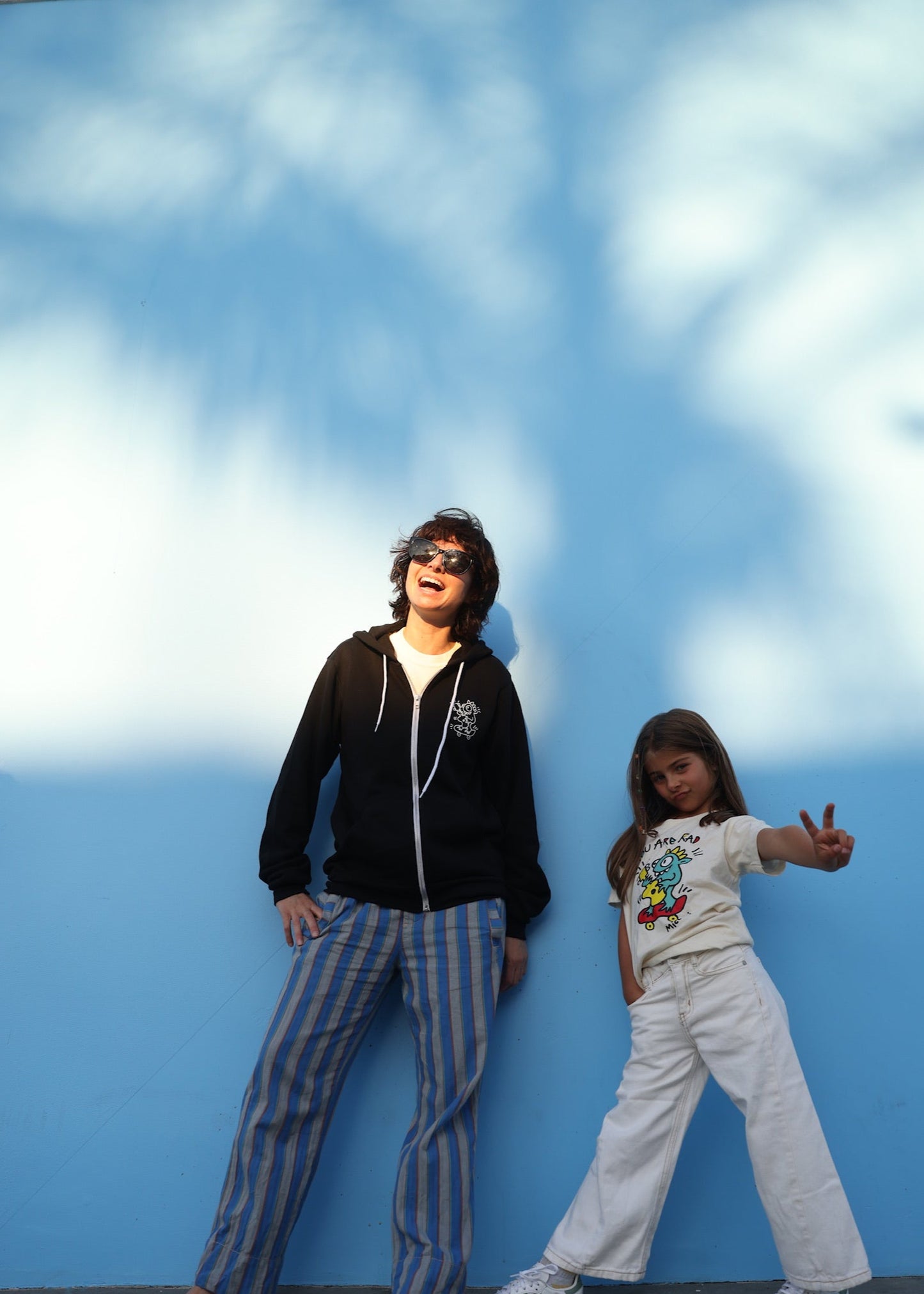 Two people posing against a blue wall with white cloud patterns