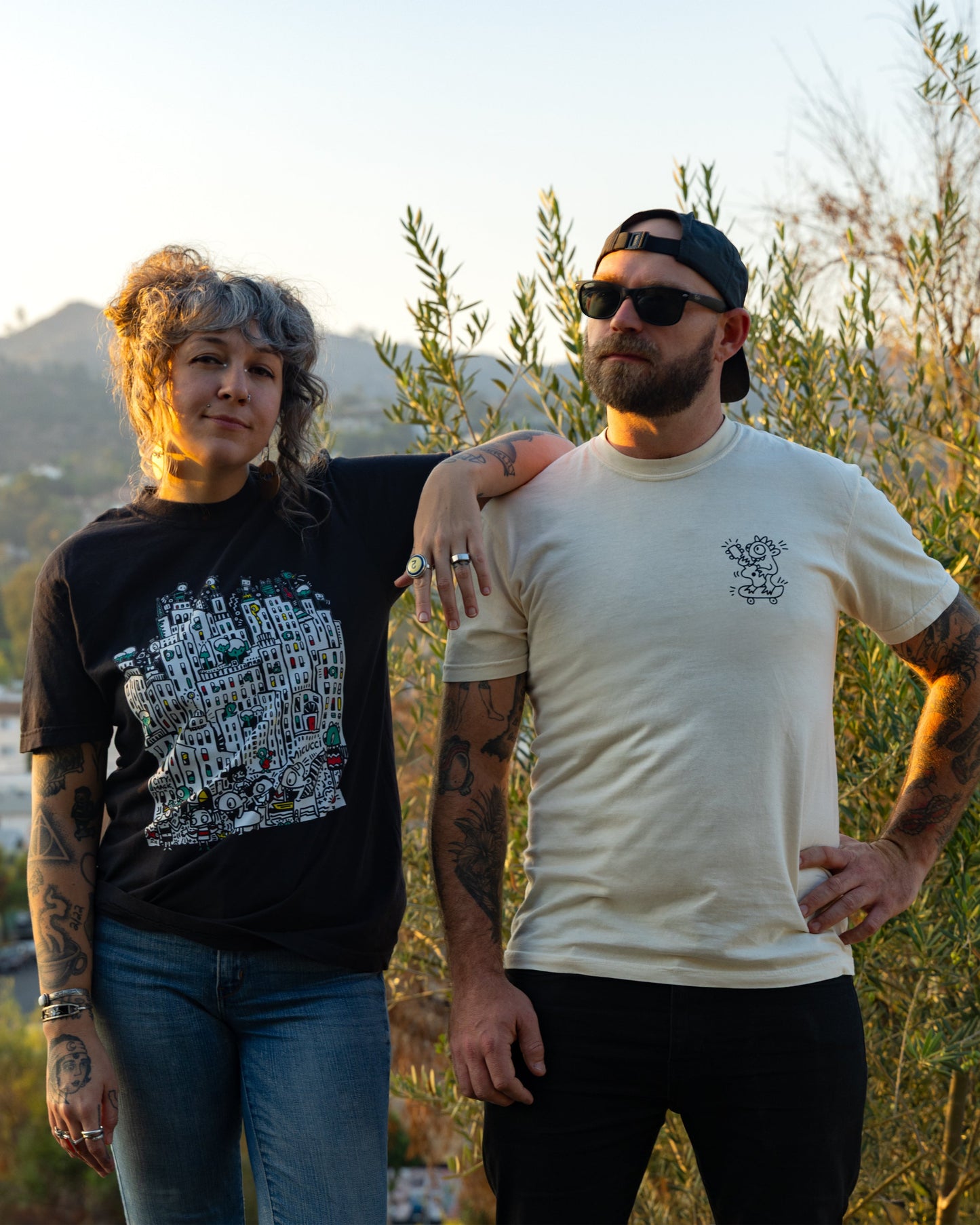 Two people standing together with a scenic background of trees and buildings.