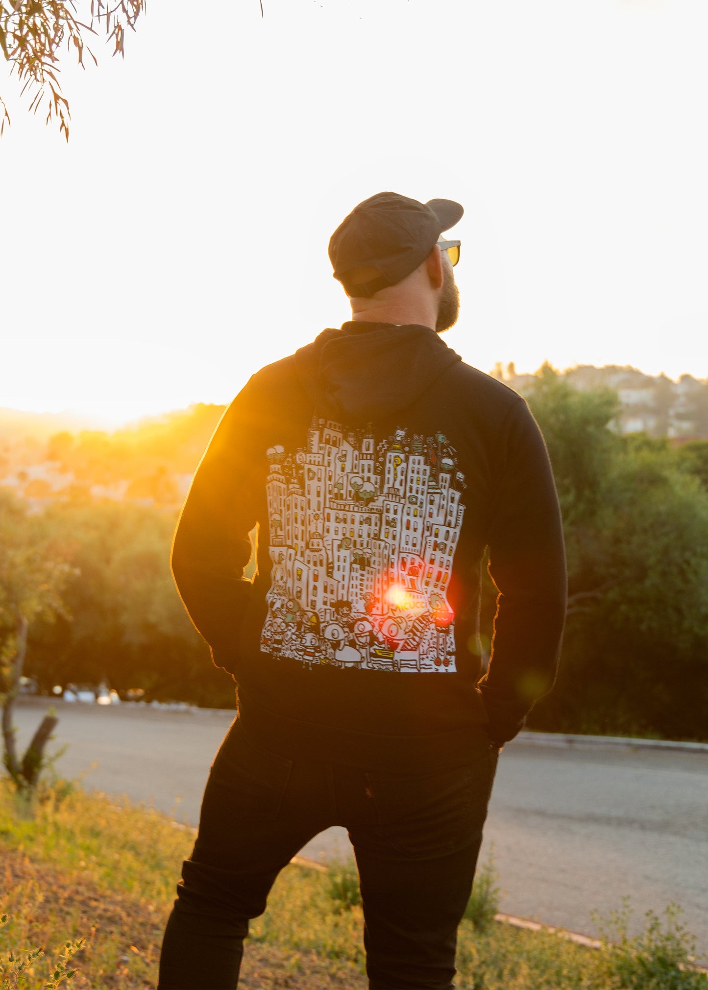 Person standing on a hill with a sunset view, wearing a jacket with a design on the back.