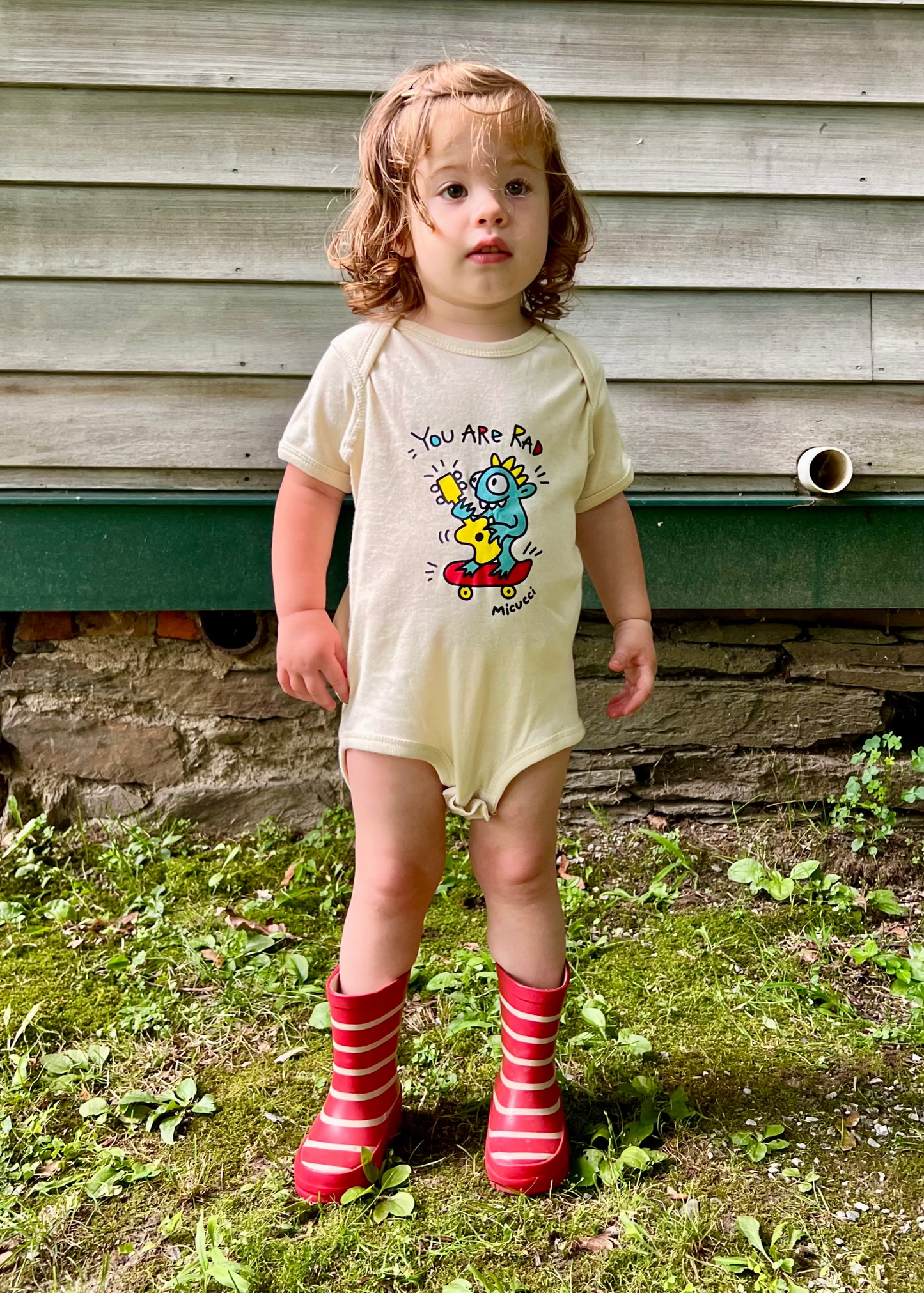 Child wearing a onesie with a cartoon design outdoors.