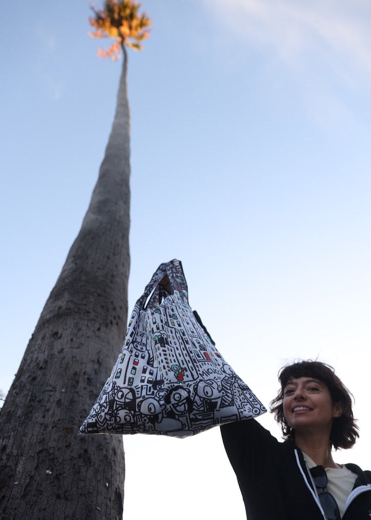 Person holding a patterned bag with a tall tree and blue sky in the background