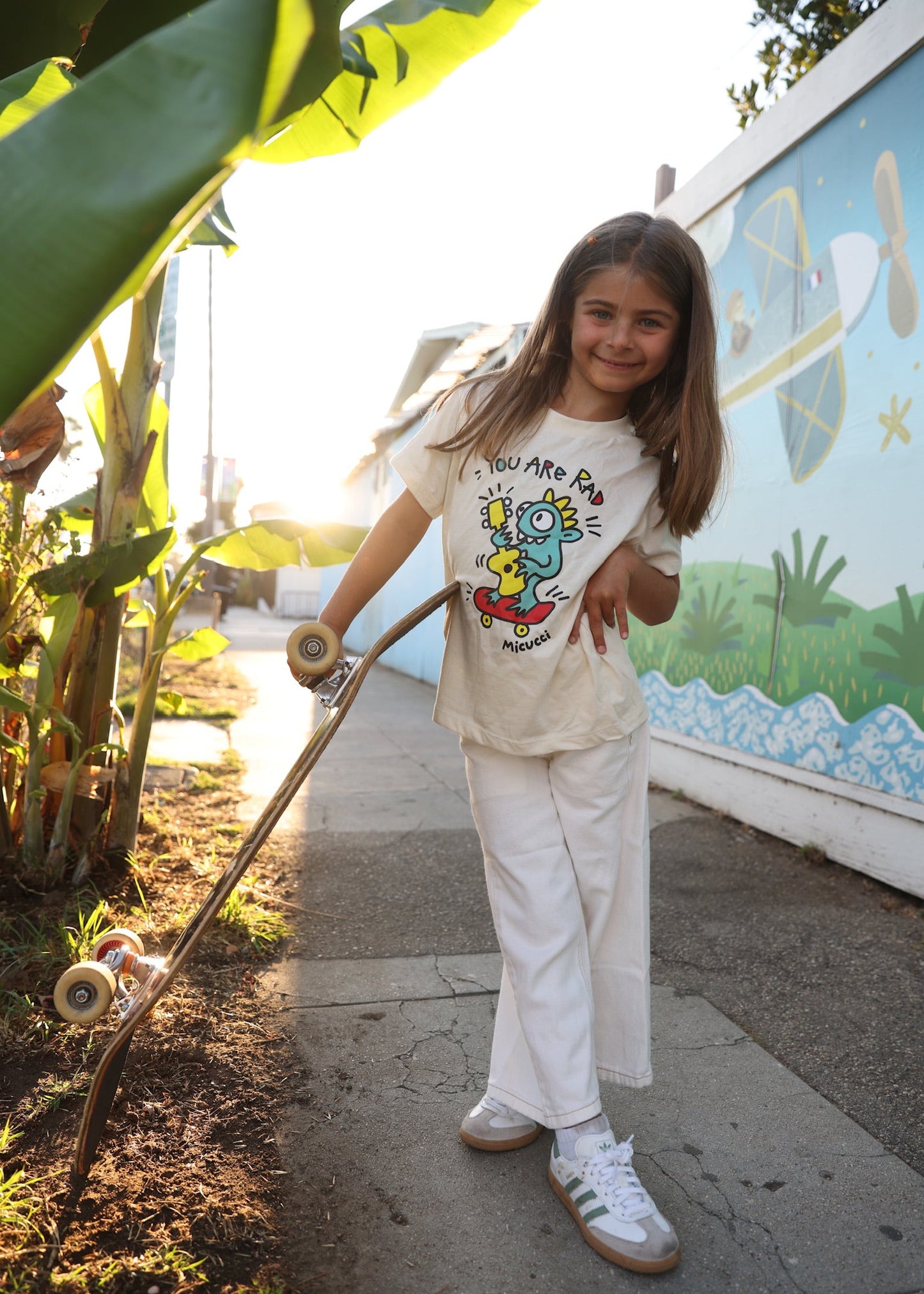 Young girl holding a skateboard with a mural in the background