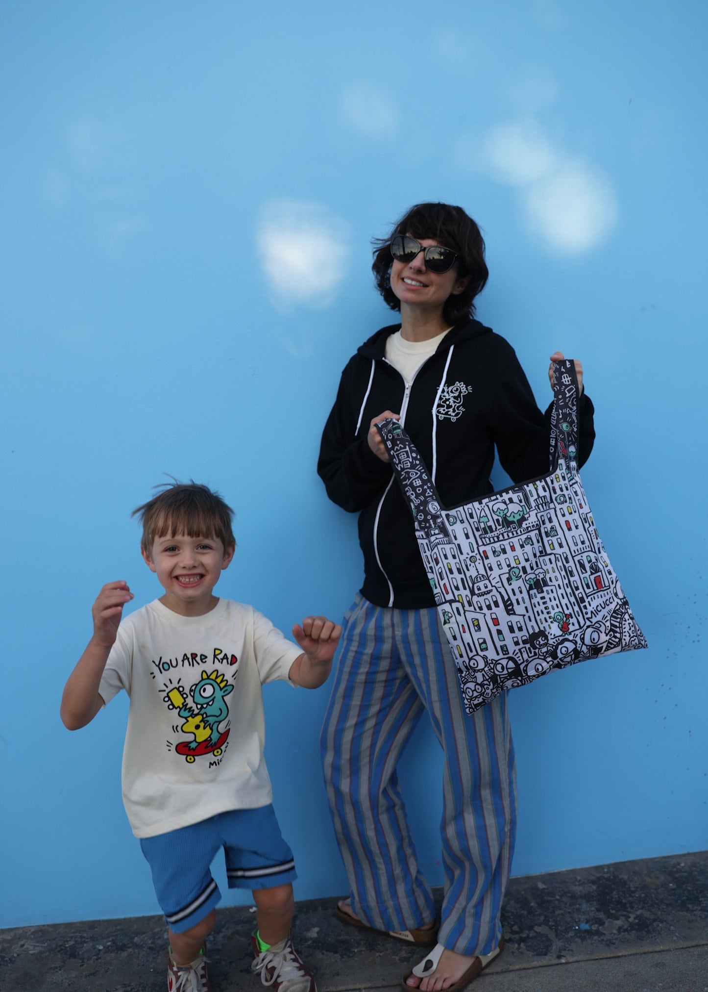 Woman and child standing against a blue wall with the woman holding a patterned bag.