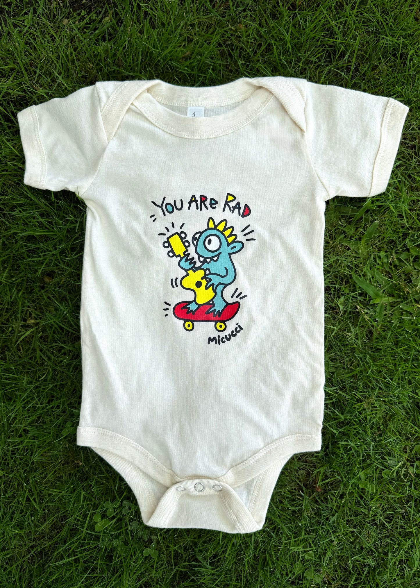 White baby onesie with cartoon design on grass