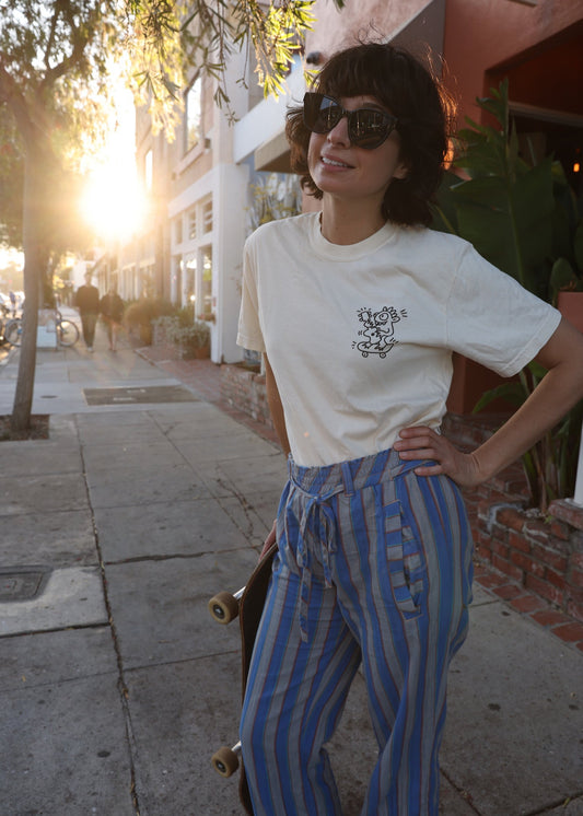 Person wearing a white t-shirt and blue striped pants standing on a sidewalk with a skateboard.