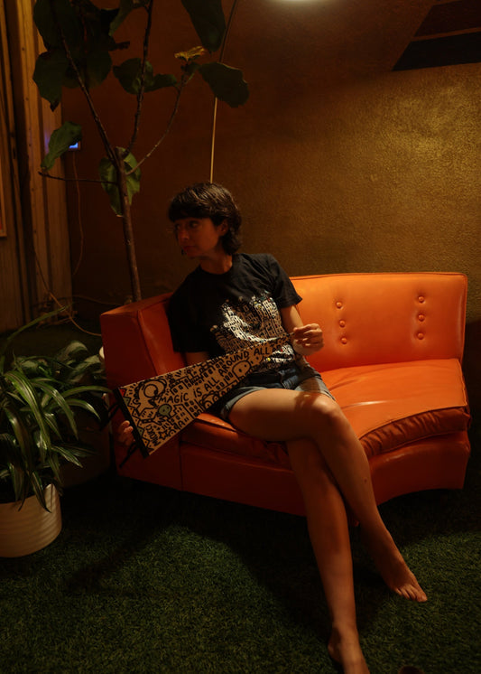 Person sitting on an orange couch in a dimly lit room with plants.