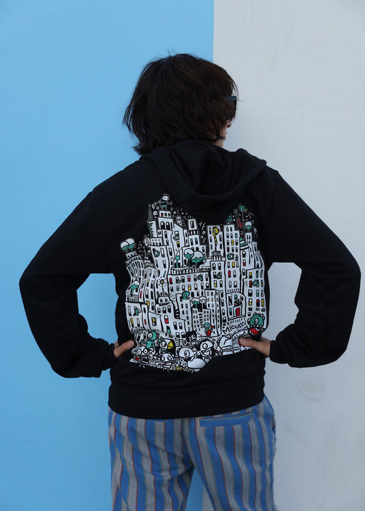 Person wearing a black hoodie with a detailed graphic on the back against a blue and white wall.